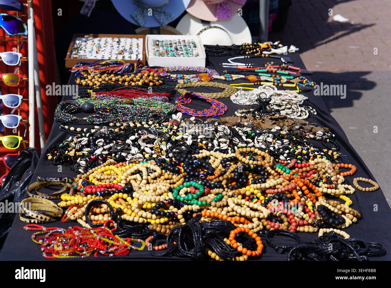 Farbenfroher Schmuckmarkt mit handgefertigten Perlen-Halsketten, Armbändern, Holzperlen und Sonnenbrillen an einem sonnigen Tag in Brighton, England. Stockfoto