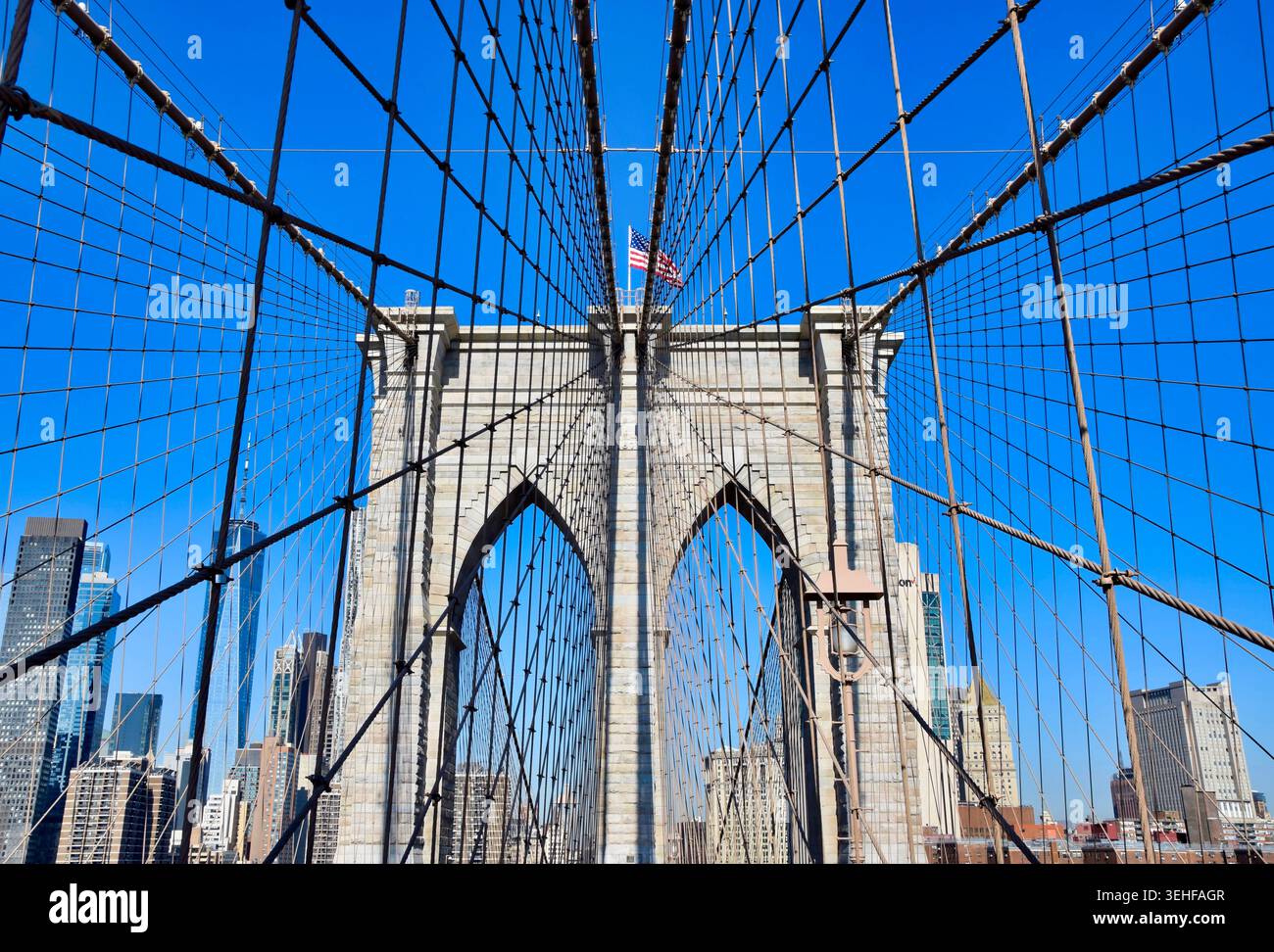Brooklyn Bridge Tower und Hängekabel aus nächster Nähe mit Manhattan Skyline und amerikanischer Flagge am klaren blauen Himmel, New York City, USA Stockfoto