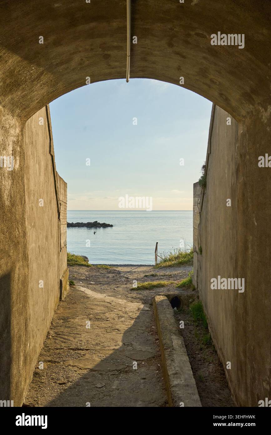 Betonbogen, der ein ruhiges Meer und einen hellen Horizont umrahmt, Licht am Ende symbolisiert Hoffnung, Freiheit und neue Reisen Stockfoto
