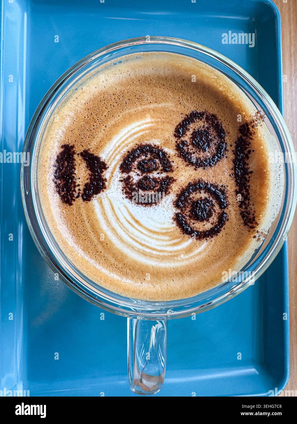 Tasse Kaffee mit dekorativem 100-Design auf dem Milchschaum, von oben auf einem hellblauen Tablett fotografiert. - Smartphone-aufgenommenes Stockfoto