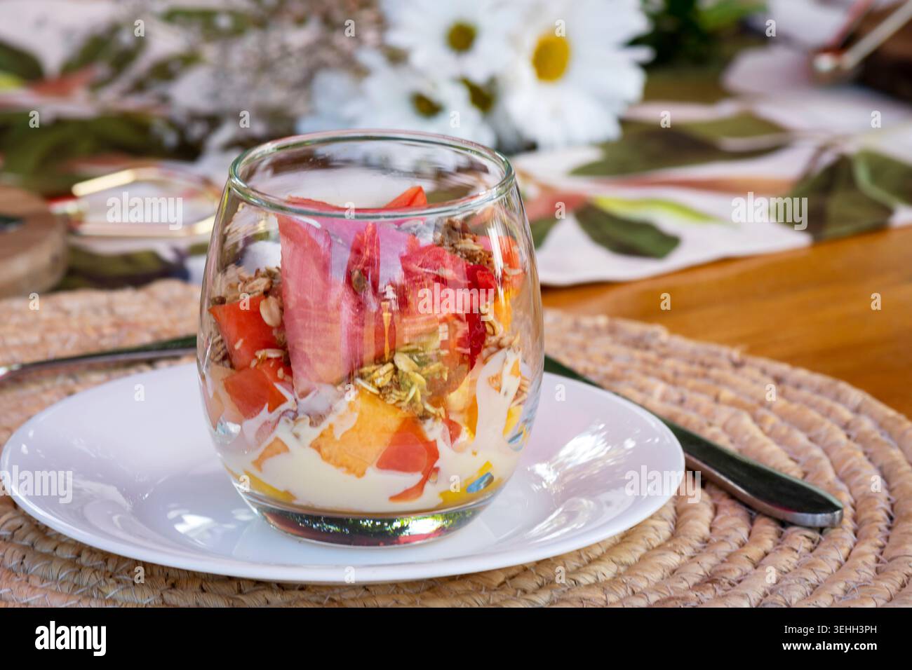 Farbenfrohes Obst-Joghurt-Parfait mit Müsli und frischer Wassermelone, serviert in einem Glas auf einem stilvollen Frühstückstisch. Stockfoto