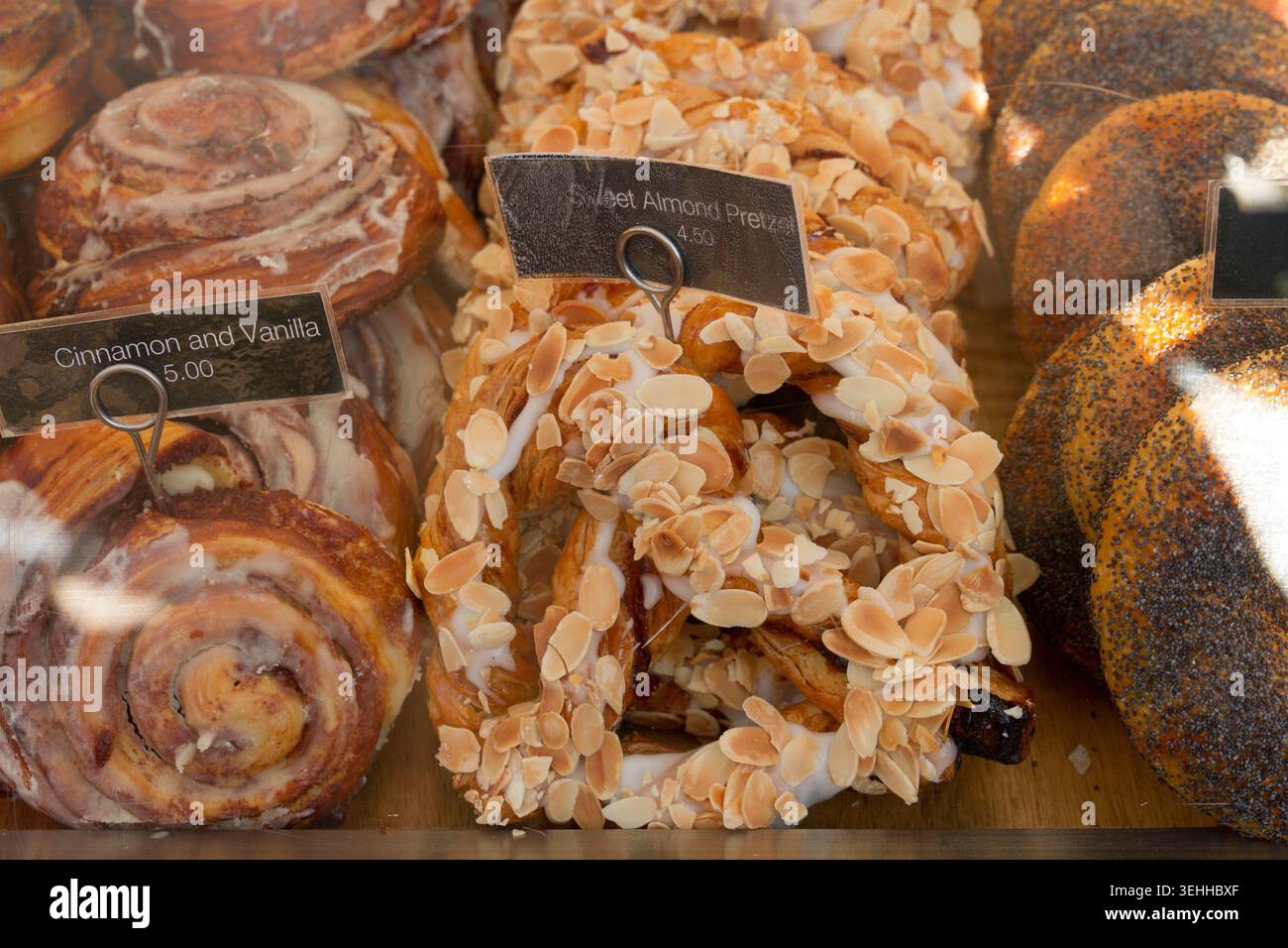 Ein Schaufenster der Bäckerei mit süßen Mandelbrezeln mit geschnittenen Nüssen und glasierten Zimt- und Vanillebrötchen. Stockfoto