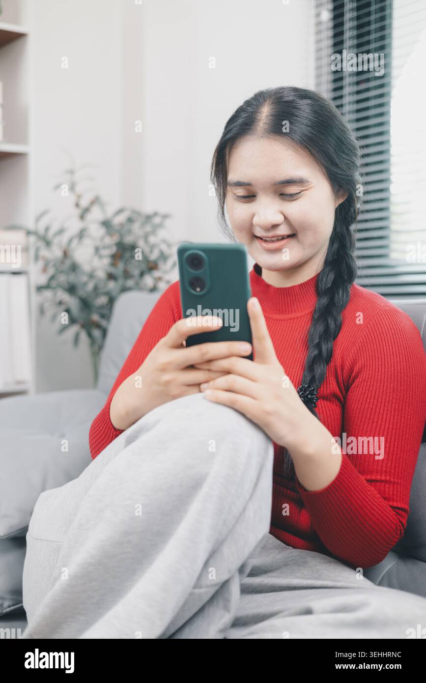 Junge asiatische Frau, die ihr Smartphone zum Online-Shopping zu Hause nutzt, mobile E-Commerce-App auf dem Sofa durchsucht, digitalen Lebensstil für Verbraucher, bequemer Kauf Stockfoto