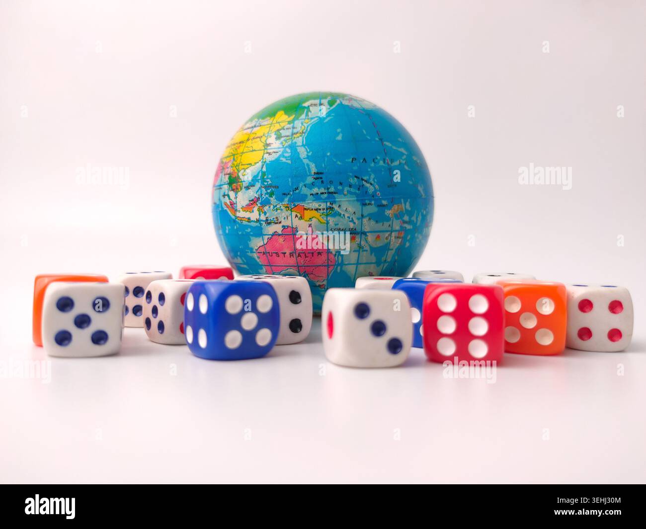 Eine kleine Spielkugel, die Australien und Asien zeigt, sitzt hinter einer Reihe von verstreuten bunten Spielwürfeln. Stockfoto