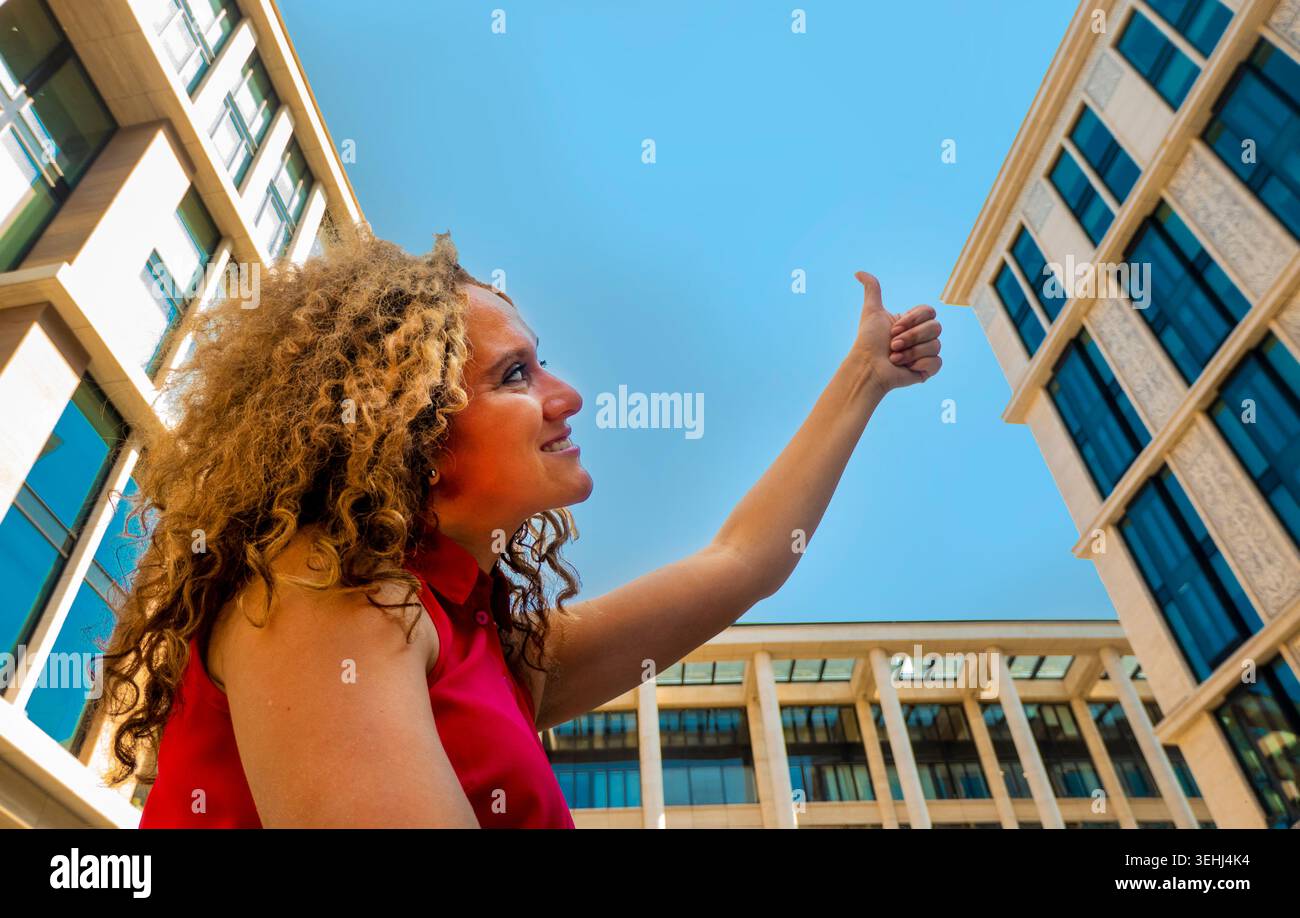 Porträt Happy Fasion Woman zeigt den Daumen nach oben gegen den Himmel und schaut seitlich und nach oben Stockfoto