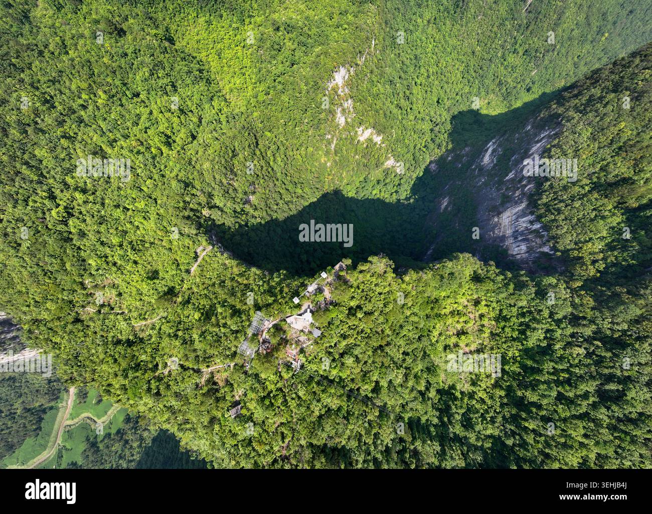 Drohnenansicht aus der Vogelperspektive eines Riesenkarstswinklochs, umgeben von dichtem Wald in der Präfektur Qiannan, Guizhou, China Stockfoto