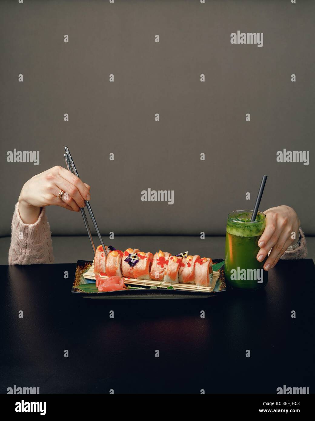 Ein Mädchen unter einem Tisch mit Essstäbchen auf dem Tisch isst Sushi und trinkt einen Cocktail. Kreativ, Werbung, Ort für Text Stockfoto