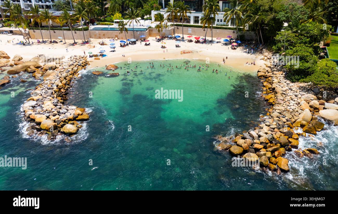Blick aus der Vogelperspektive auf Playa Esmeralda mit einer türkisfarbenen Bucht mit schwimmenden Menschen und einem felsigen Wellenbrecher in Puerto Vallarta, Jalisco, Mexiko. Stockfoto