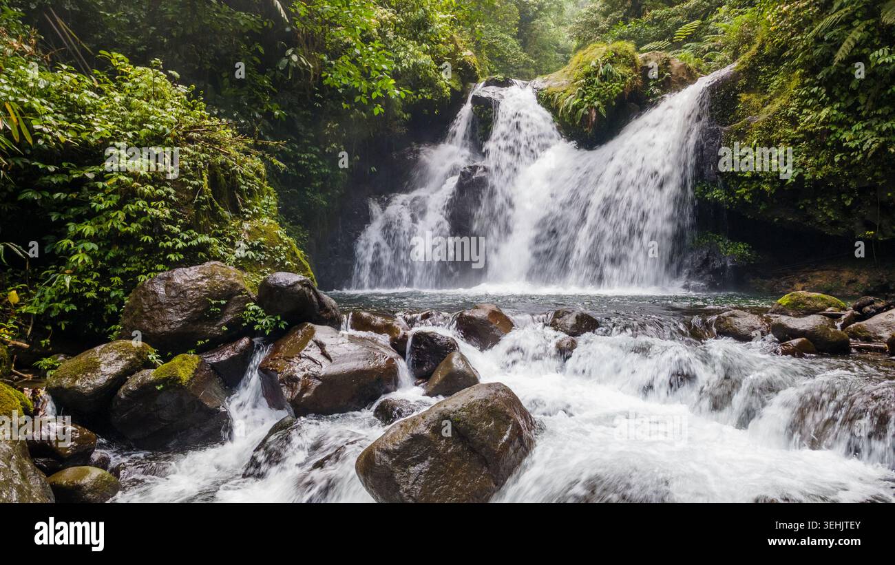 Aus der Vogelperspektive des Ambyar Wasserfalls, der über dunkle moosige Felsen stürzt, umgeben von dichtem tropischem Wald in Purwokerto, Zentral-Java, Indonesien. Stockfoto