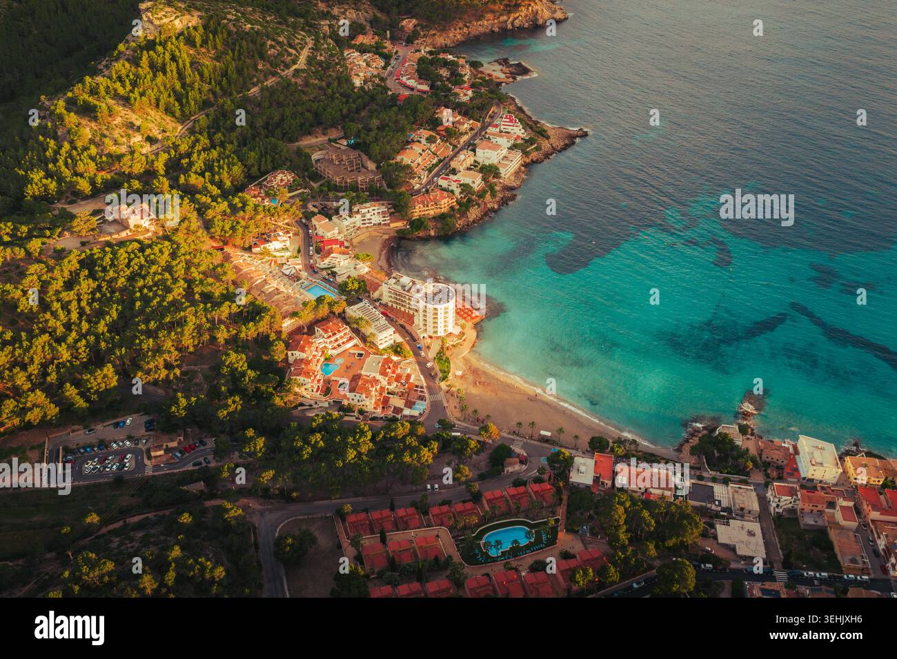 Blick aus der Vogelperspektive auf die Küstenstadt mit türkisfarbenem Wasser, Sandstrand und üppigen grünen Kiefernwäldern unter der goldenen Stunde Sant Elm, Balearen Isla Stockfoto