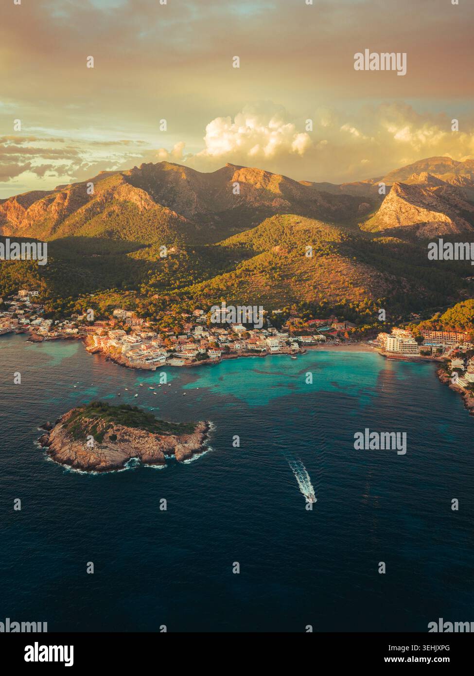 Aus der Vogelperspektive auf das Küstendorf Sant Elm mit seiner türkisfarbenen Bucht, einer kleinen felsigen Insel und den zerklüfteten Tramuntana Bergen unter einem warmen Sonnenuntergang Stockfoto
