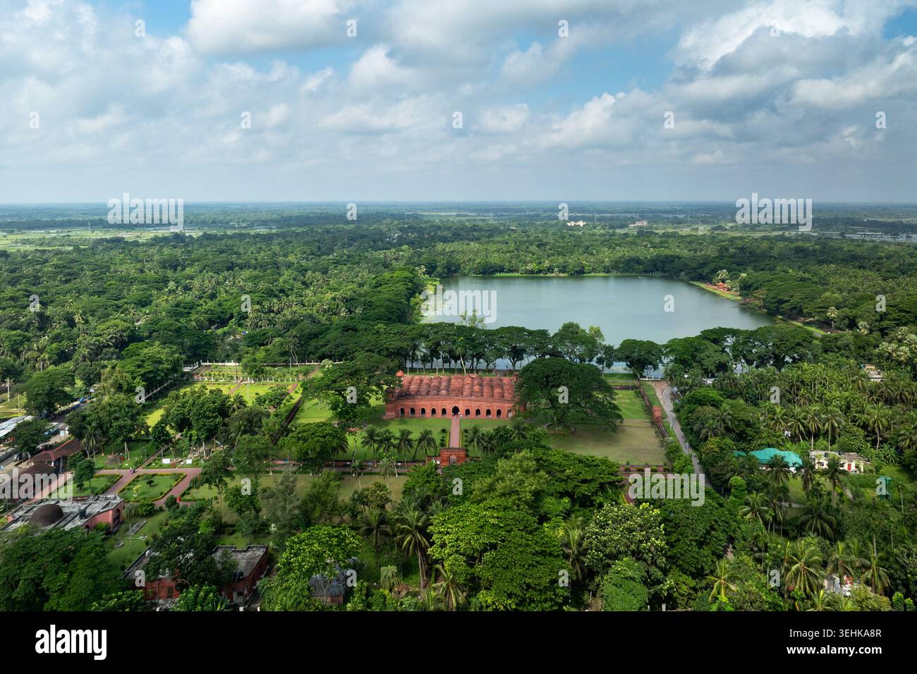 Blick aus der Vogelperspektive auf die historische Sixty Dome Moschee, umgeben von üppigen grünen Bäumen und einem großen Teich unter einem bewölkten Himmel in Bagerhat, Khulna Division, Banglad Stockfoto