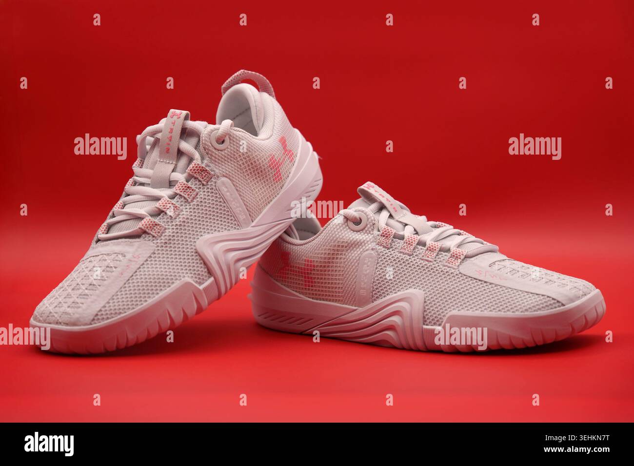 Ein Paar sportliche Under Armour TriBase Reign 6 Trainingsschuhe in weiß und hellrosa mit einem leuchtend roten Hintergrund Stockfoto