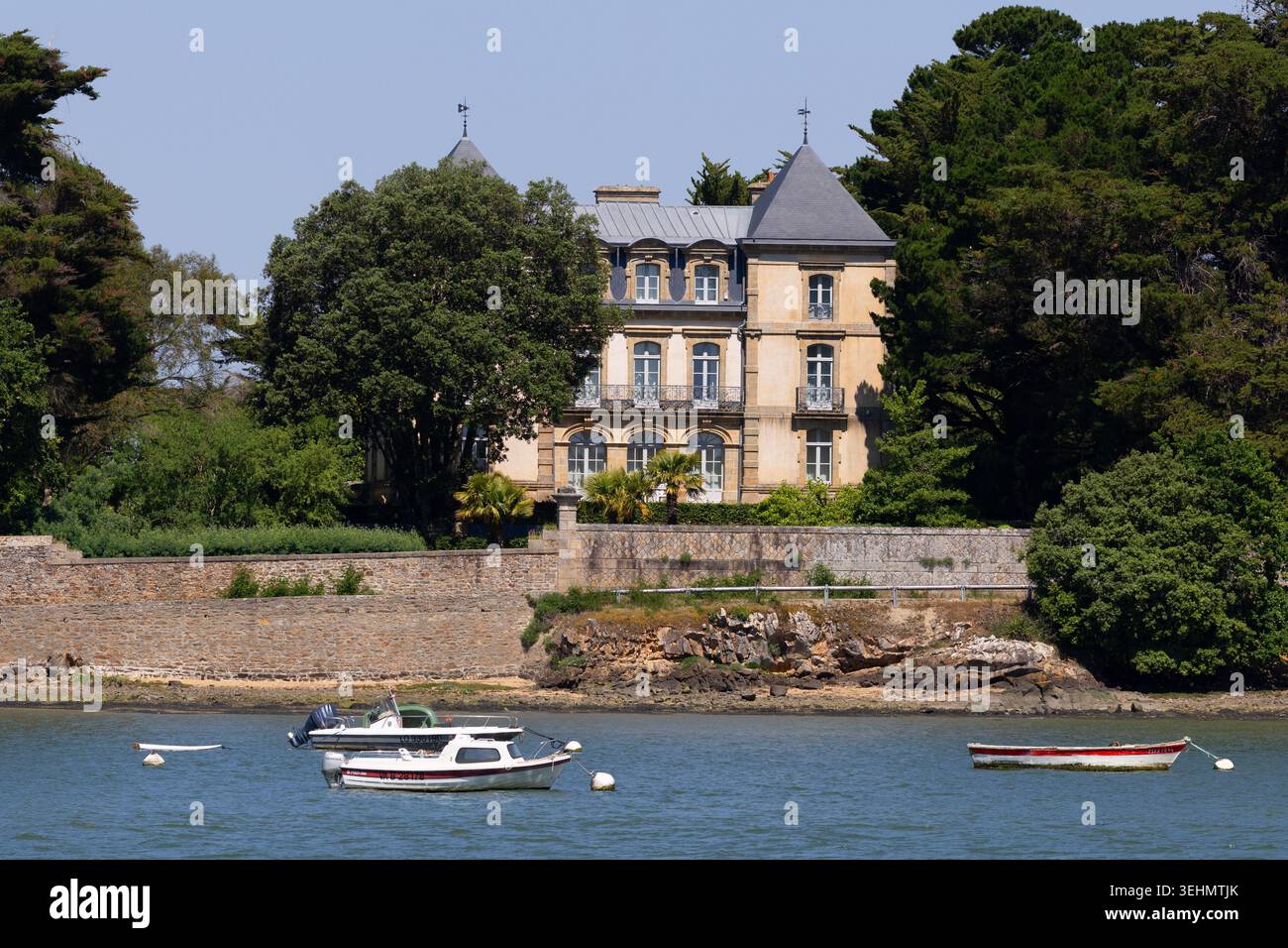 Großes Haus am Ufer des Golfe du Morbihan mit kleinen Booten im Vordergrund, Bretagne, Frankreich. Stockfoto