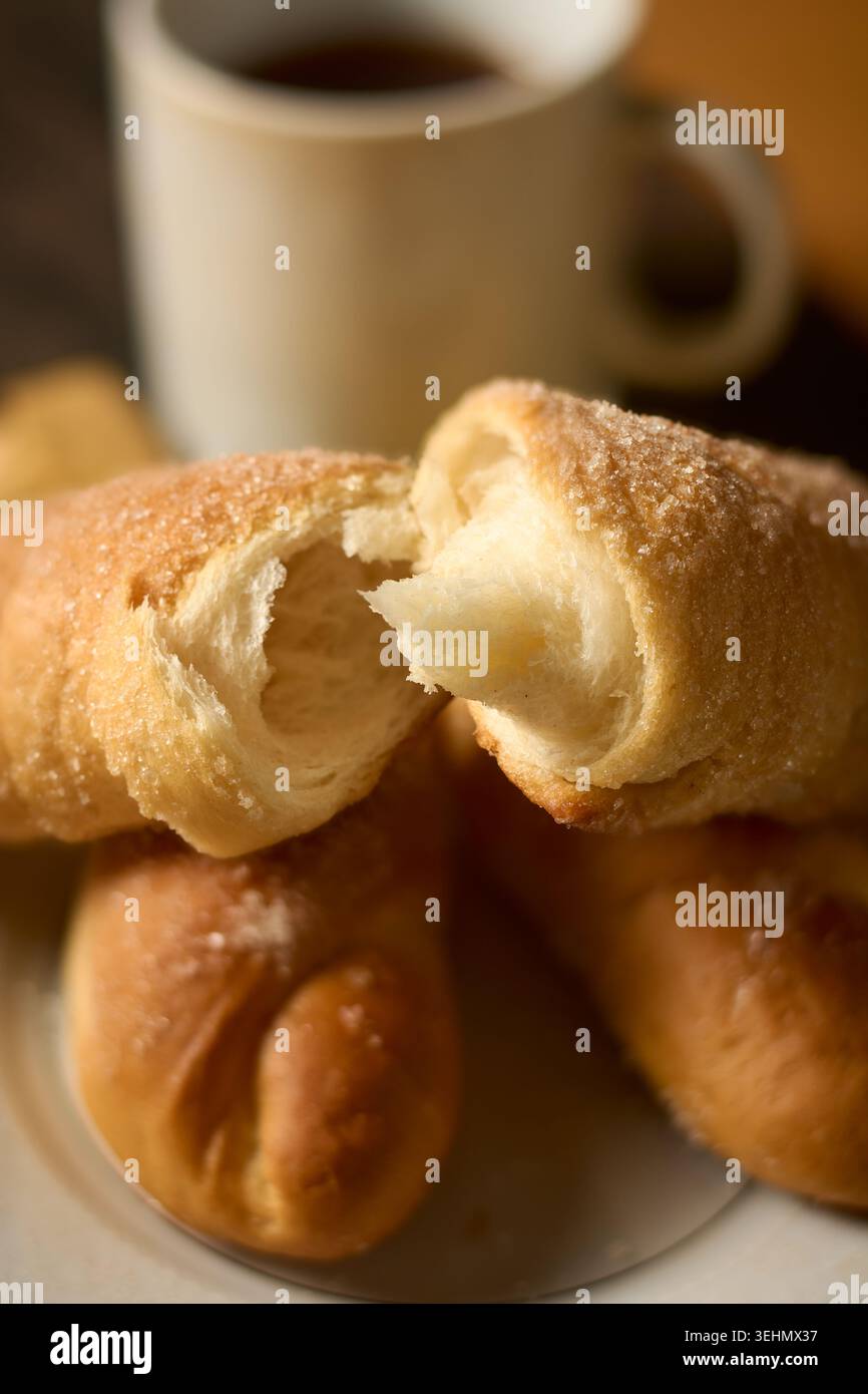 Mit Zucker überzogene Kibula Banis auf weißer Platte, Spiralgebäck mit weichem weißem Brot im Inneren mit verschwommenem Becher, Seitenansicht mit weichem Fokus Stockfoto