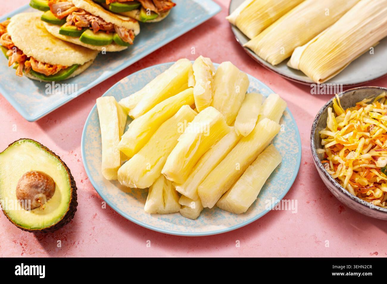 Gekochter Yuca in der Mitte eines farbenfrohen lateinamerikanischen Esstisch mit Pupusas, Humitas, Curtido und Avocado, gestylt für ein festliches Weihnachtsessen. Stockfoto