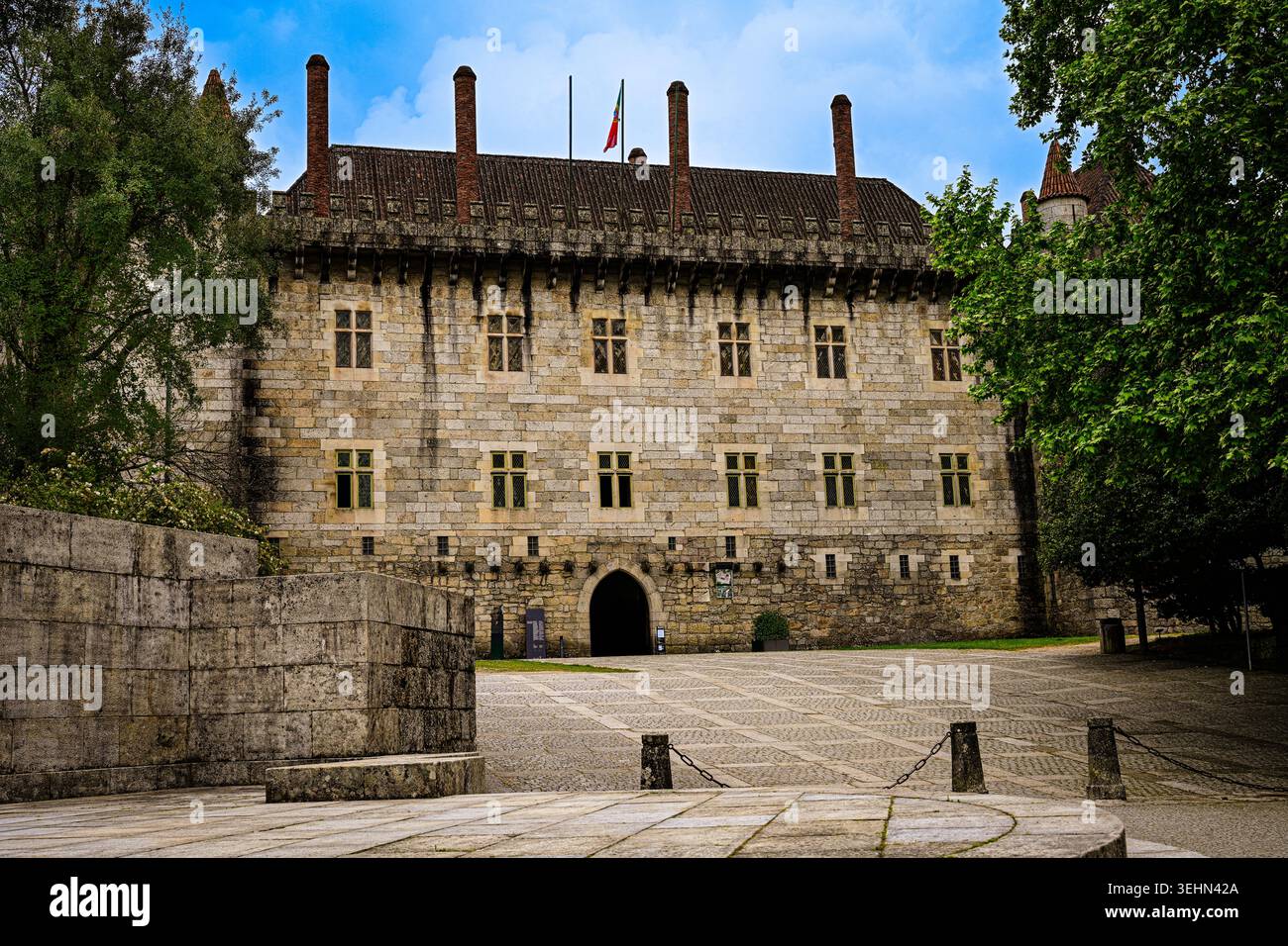 Ein mittelalterlicher Steinpalast mit hohen Schornsteinen und historischer Architektur steht in einem ruhigen Innenhof in Guimarães, Portugal. Stockfoto