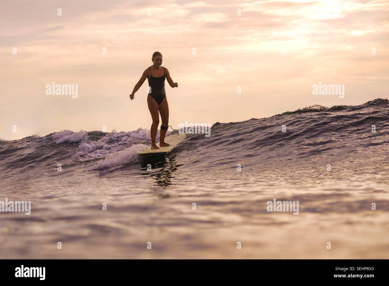 Frau Tanzt Auf Surfbrett Unter Sonnenuntergang, Arme In Celebration Erhoben, Während Sie Sanfte Schwellen Reiten, Verspielter Rhythmus, Stockfoto