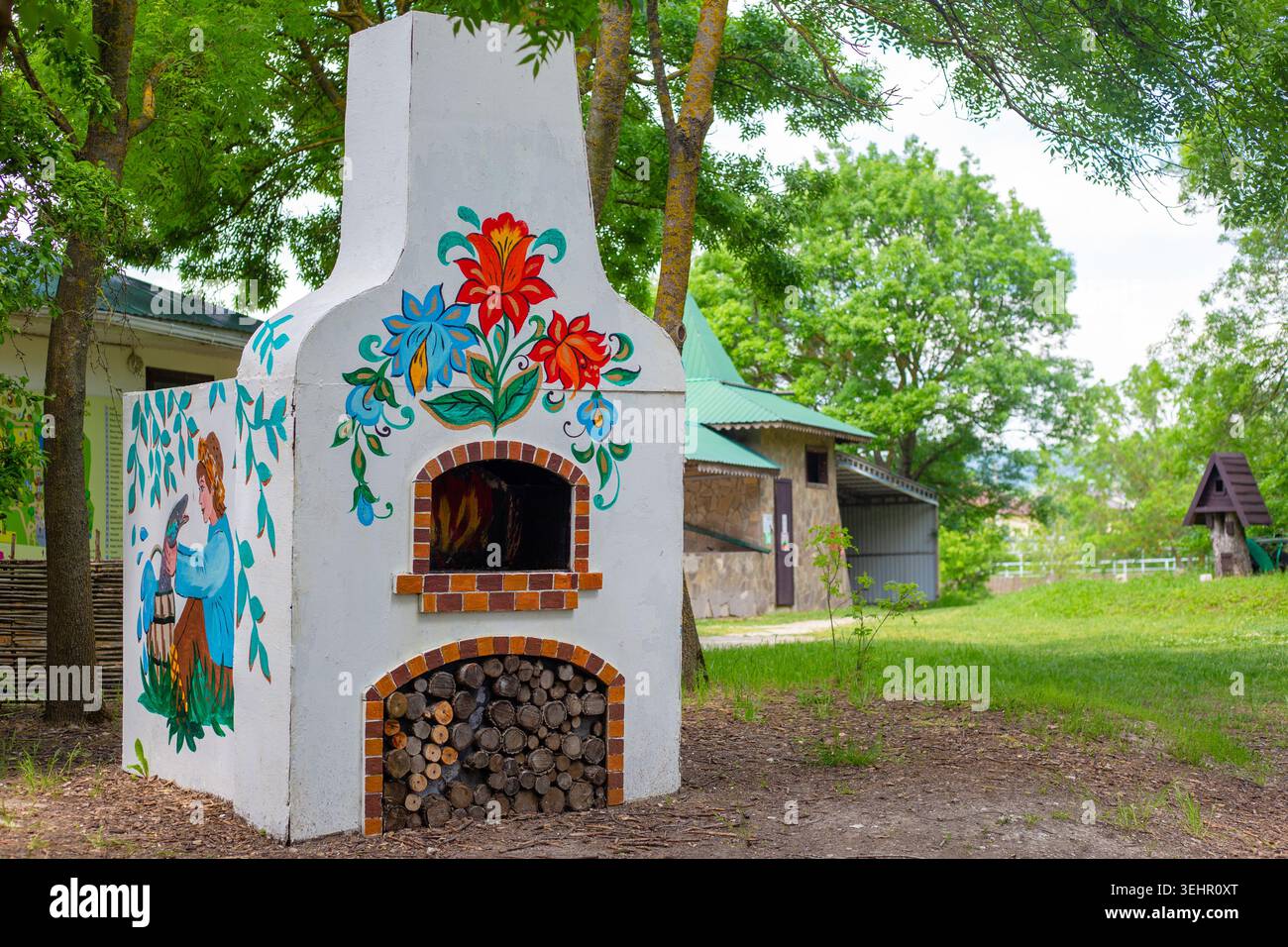 Ein traditioneller Steinofen im Freien, dekoriert mit bunten bemalten Blumen in einem grünen Garten. Rustikaler Kamin, ethnische Einrichtung, Hinterhof-Design. Stockfoto