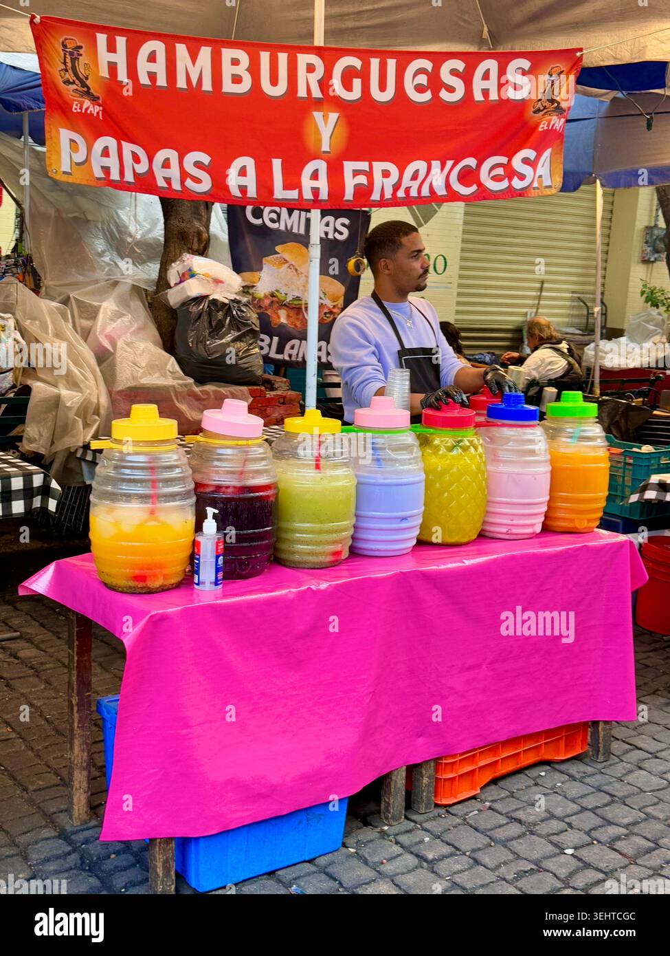 Ein Händler verkauft Hamburger, Pommes Frites und farbenfrohe aguas Frescas im Mercado de Antojitos Mexicanos in Coyoacán, Mexiko-Stadt Stockfoto