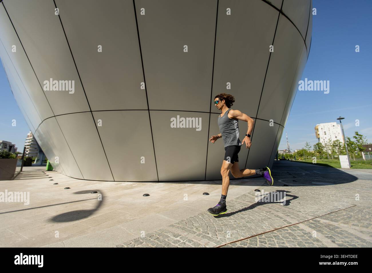 Ein entschlossener Athlet sprintet auf einem glatten Weg und zeigt an einem sonnigen Tag Stärke vor einem Hintergrund eines eleganten, futuristischen Designs. Stockfoto
