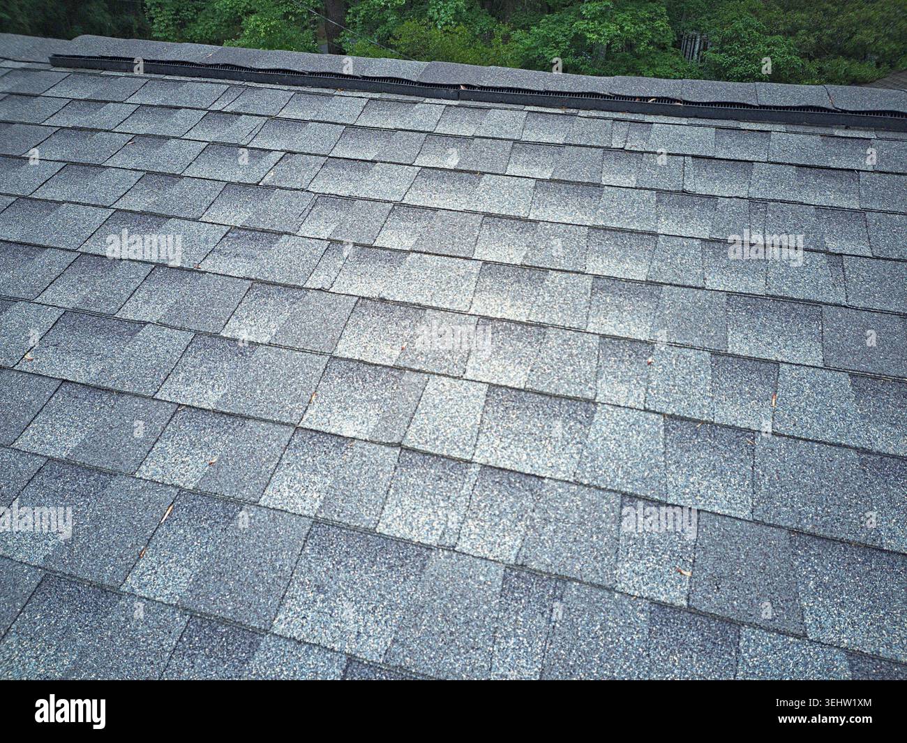 Detaillierte Perspektive eines verwitterten grauen Asphaltschindeldachs, das die Firstkappe und das integrierte Belüftungssystem zeigt. Stockfoto