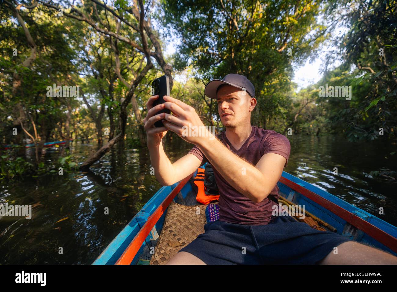 Touristen im Boot, die mit dem Handy Fotos von Bäumen machen, die aus dem Wasser auf dem Tonle SAP See Kambodscha wachsen. Ökotourismus, Reisefotografie, schwimmende Villa Stockfoto