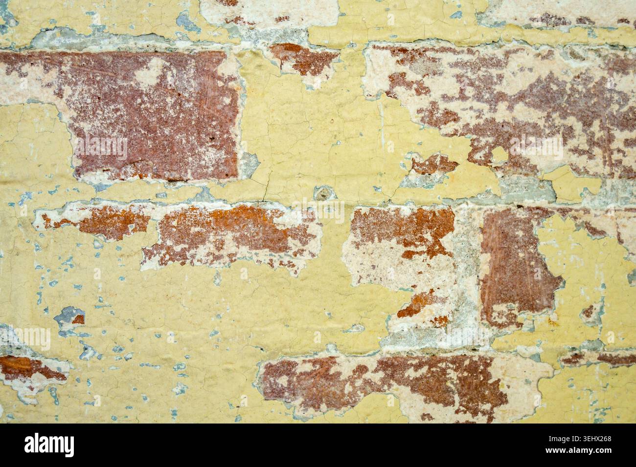 Nahansicht der rustikalen Ziegelwand mit abblätternder gelber Farbe. Stockfoto