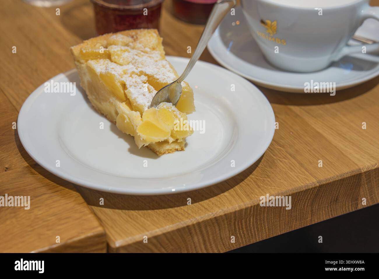 Ein Stück Apfelkuchen auf einem Teller neben einer Tasse auf einem Holztisch in einem gemütlichen Café, Cafe Kuh, Deckenpfronn, Deutschland Stockfoto