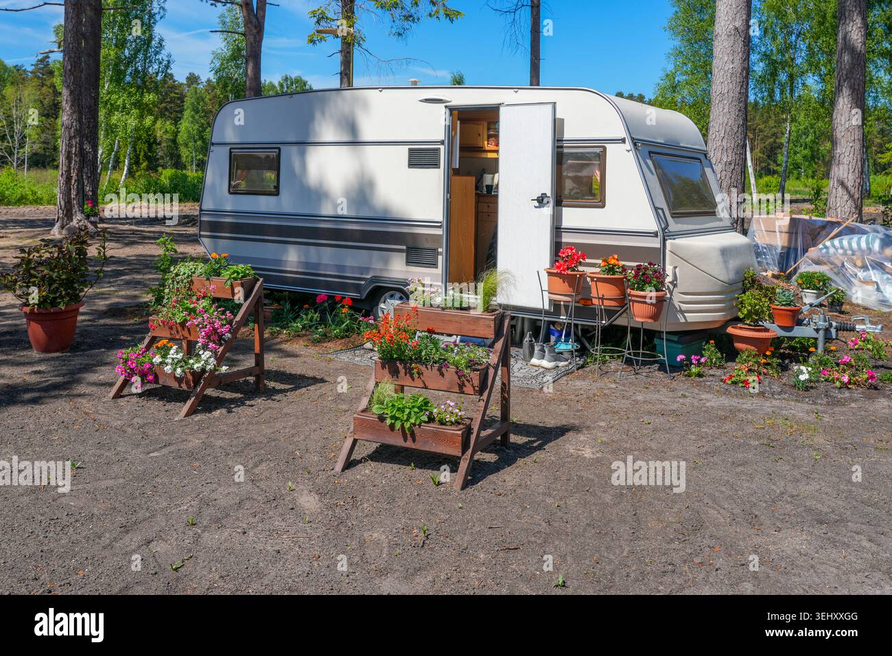 Gemütlicher Wohnmobil mit farbenfrohem Blumengarten auf dem Waldcamping an sonnigen Sommertagen Stockfoto