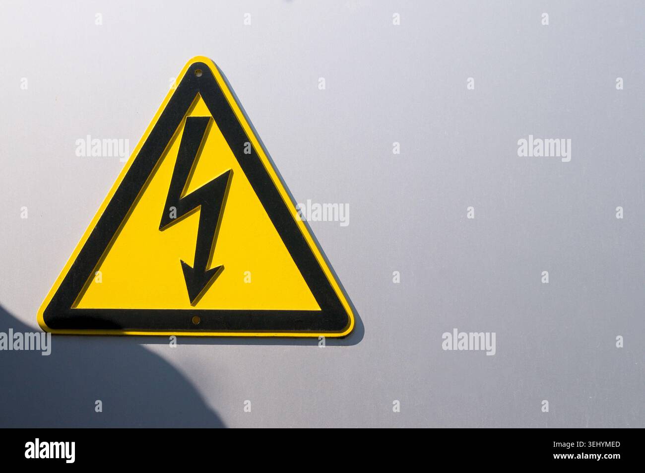 Nahaufnahme eines Warnschilds für Hochspannungsgefahr mit gelbem Blitzsymbol an einem Maschendrahtzaun. Konzept für elektrische Gefahren, Stromversorgung Stockfoto