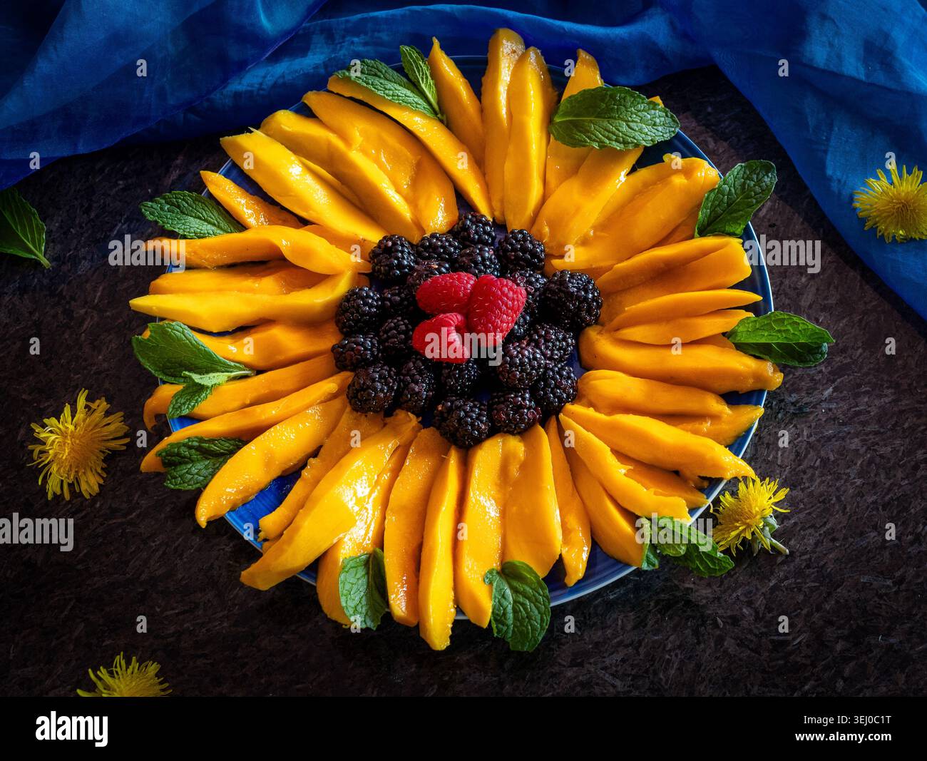 Eine optisch atemberaubende und gesunde Obstplatte in Form einer Sonnenblume angeordnet. Die künstlerische Präsentation zeigt lebendige Mangobeigen als Blütenblätter, Stockfoto
