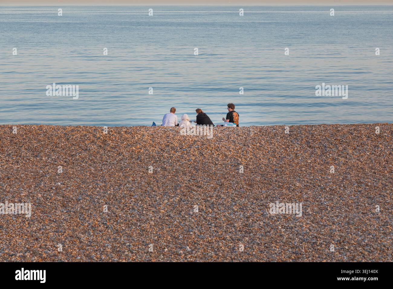 Eine vierköpfige Familie, die sich an einem Kieselstrand am ruhigen blauen Meer entspannt. Stockfoto