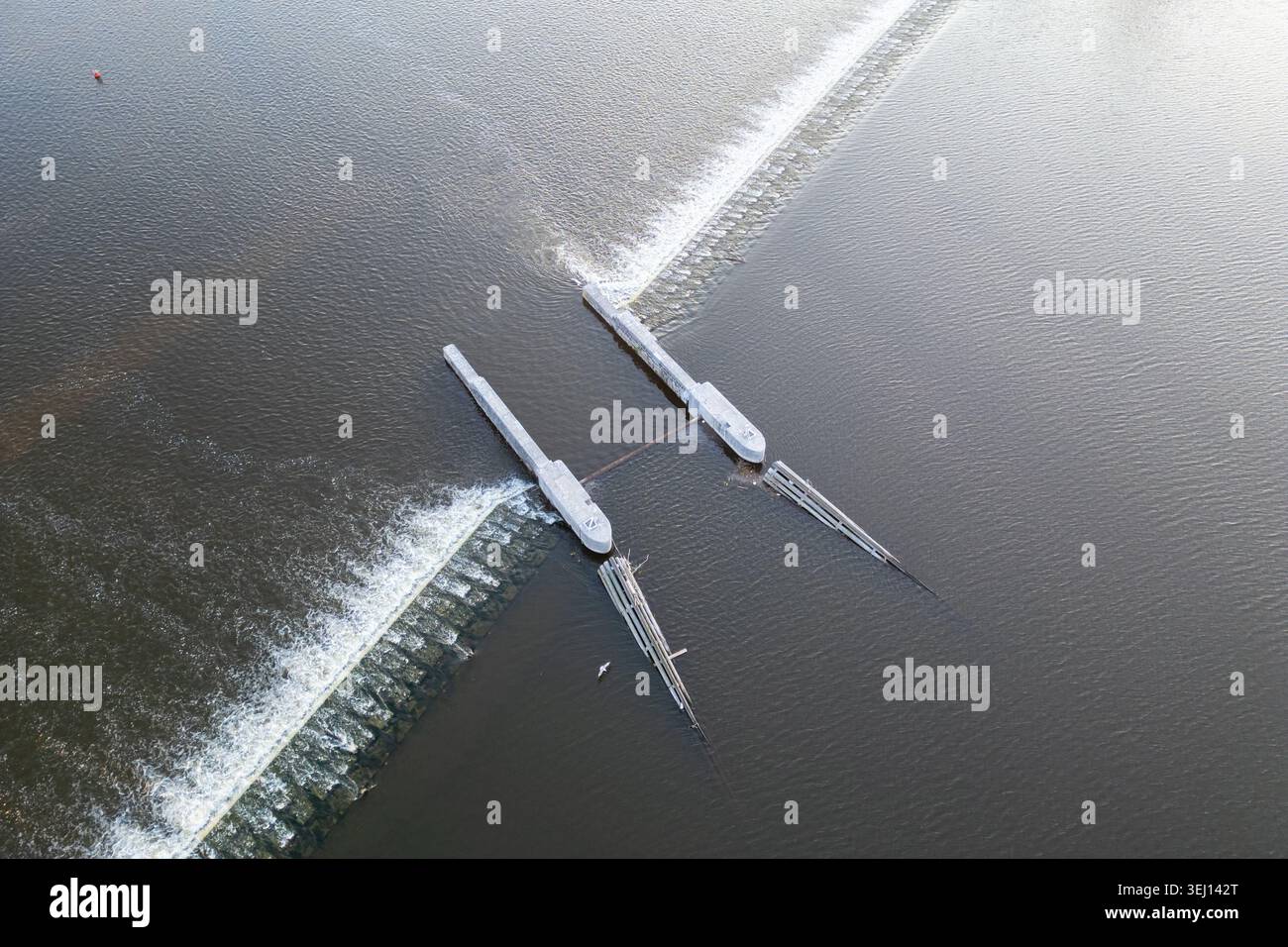 Das Bild zeigt ein Wehr auf der Moldau in Prag. Wasser fließt über die Struktur, während Boote in der Nähe vorbeifahren. Die Szene zeigt die Aktivitäten am Tag entlang des Flusses. Stockfoto