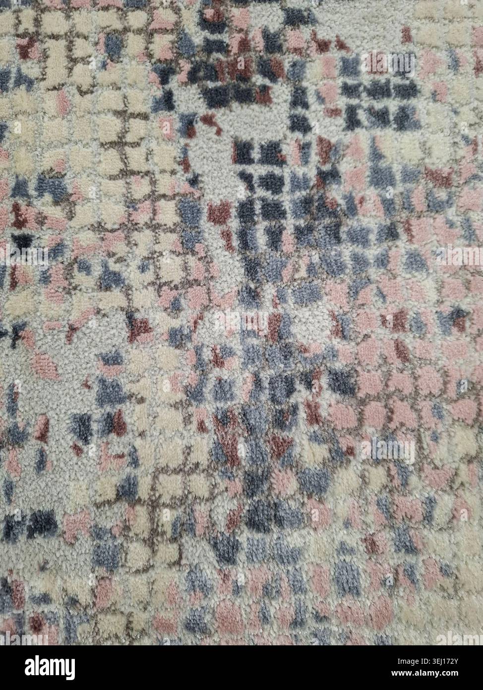 Die Ansicht zeigt einen Plüschteppich mit einem abstrakten, pixelförmigen Muster aus Creme-, Rosa- und marineblauen Farben. Der Teppich wird auf einer Ebenen Fläche aufgestellt, hoch Stockfoto