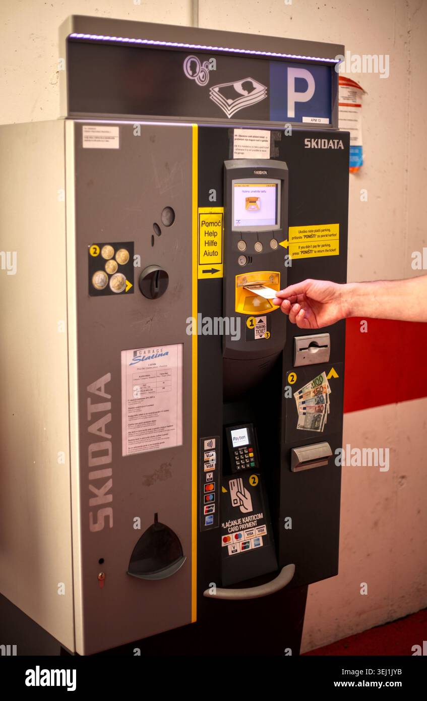 Eine Person, die ein Barcode-Parkticket in ein automatisiertes Zahlungsterminal von Skidata in der Garage von Slatina in Opatija, Kroatien, einfügt. Stockfoto