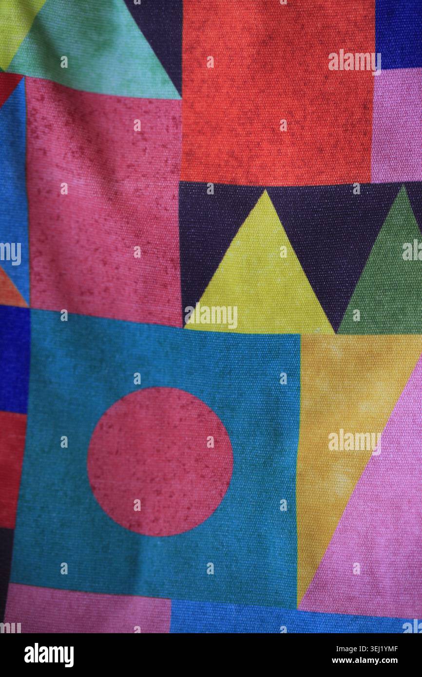 Farbenfrohes geometrisches Stoffmuster mit abstrakten Dreiecken, Quadraten und Kreisen in knalligen Rosa-, Blau-, Gelb- und Rottönen. Modernes Textildesign Stockfoto