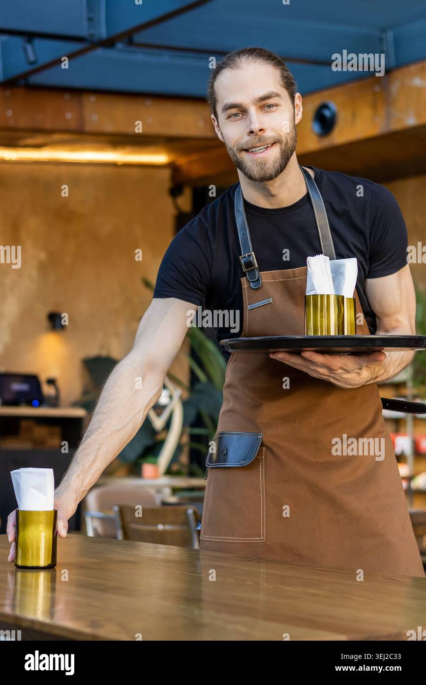 Porträt eines lächelnden Kellners, der einen Tisch im Café legt Stockfoto