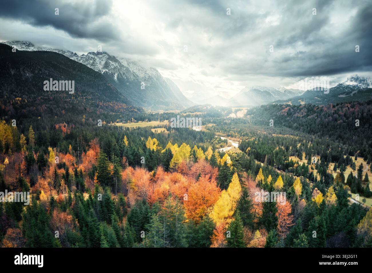 Farbenfroher, malerischer Herbstwald mit dramatisch bewölktem Himmel und Bergen im Hintergrund, Blick aus der Luft Stockfoto