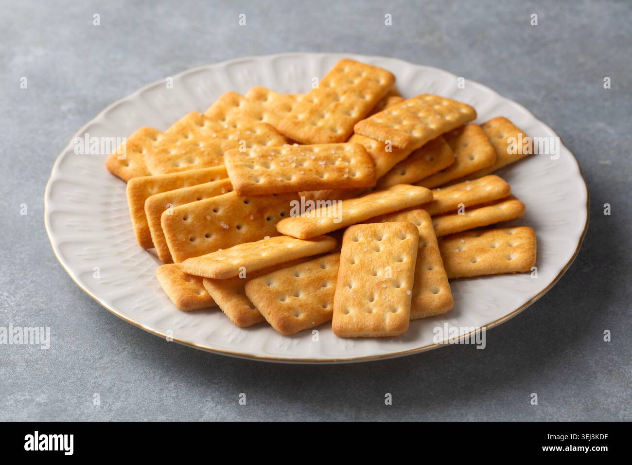 Knusprige goldene, gesalzene Cracker stapeln sich auf einer weißen Keramikplatte Stockfoto