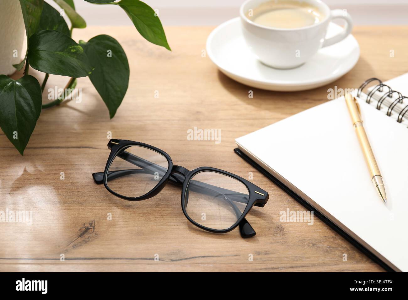 Zwei stilvolle Gläser, Notizblock und Tasse Kaffee auf Holztisch drinnen, Nahaufnahme Stockfoto