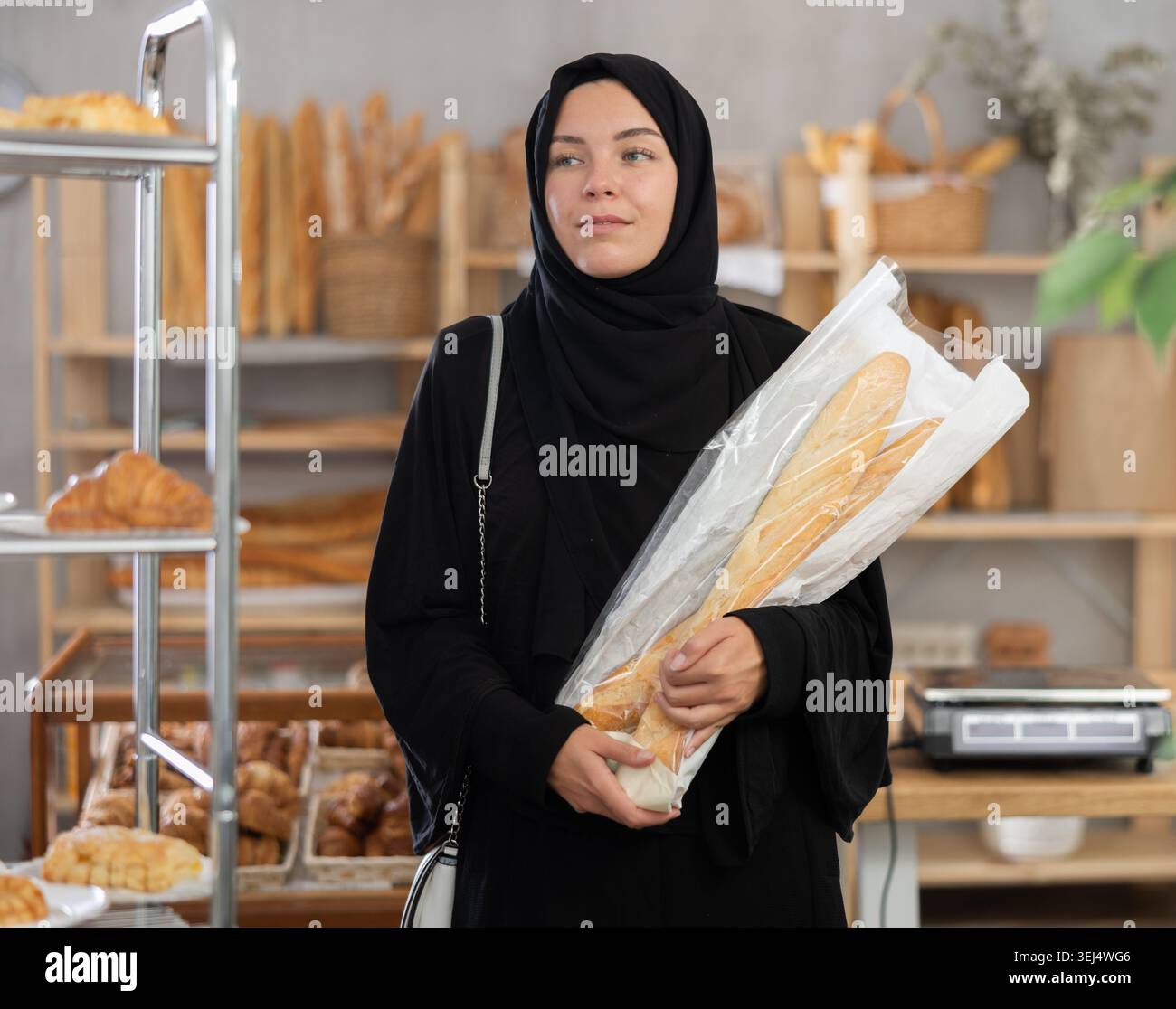 Porträt eines orientalischen Mädchens in Abaya mit frischen Baguettes in der Hand in der Bäckerei Stockfoto