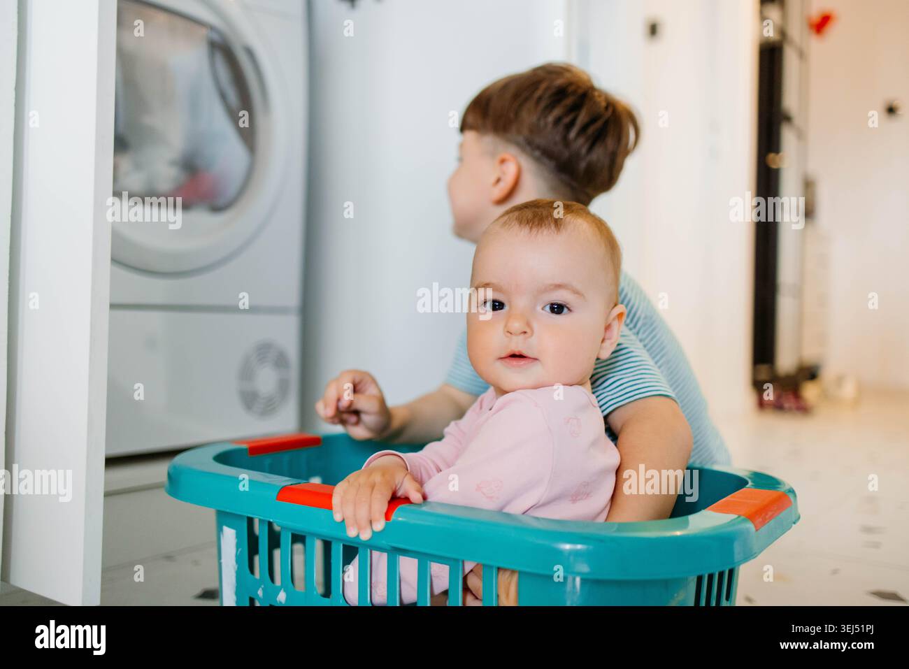 Geschwister verbringen Zeit in Waschküche, Badezimmer, Bruder fährt Schwester in Wäscheschale, Stockfoto