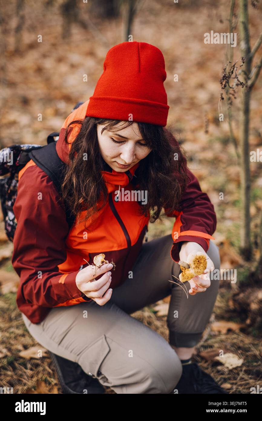 Frau hockt sich im Wald und untersucht kleine Wildpilze. Überlebenstechniken im Freien, Primitivfähigkeitstraining, Selbstständigkeit in der Wildnis, Buschkunst Stockfoto