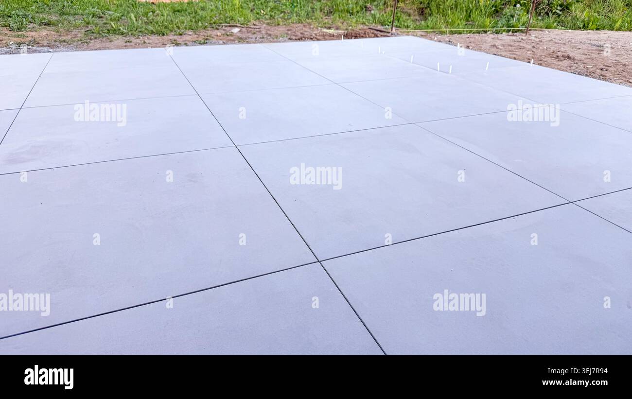 Glatte graue Betonoberfläche mit sichtbaren Fugen und grasbewachsenem Bereich im Hintergrund Stockfoto