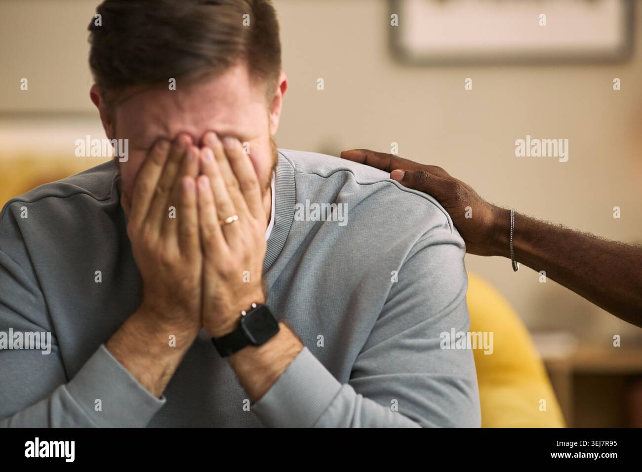 Nahaufnahme eines kaukasischen jungen erwachsenen Mannes, der das Gesicht bedeckt, während ein männlicher Freund ihn mit Hand auf Schulter tröstet und emotionale Unterstützung ausdrückt. Ideal für psychische Gesundheit, Freundschaft, Beratung Stockfoto
