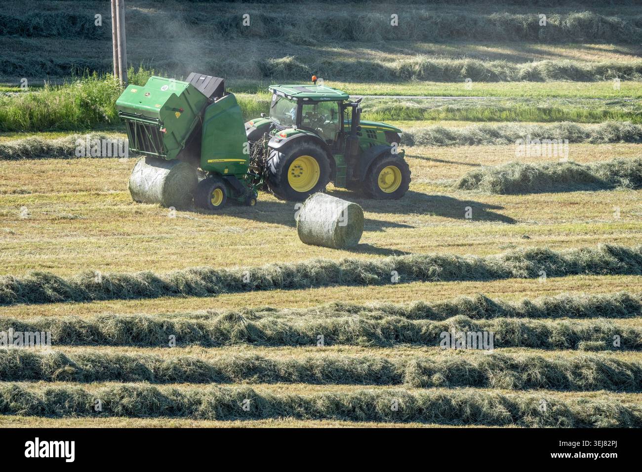 Heuernte im Wodantal: Ein John Deere-Traktor zieht eine John Deere-Rundballenpresse und nimmt das Erntegut auf – Stroh, das zuvor gemäht wurde, dr Stockfoto