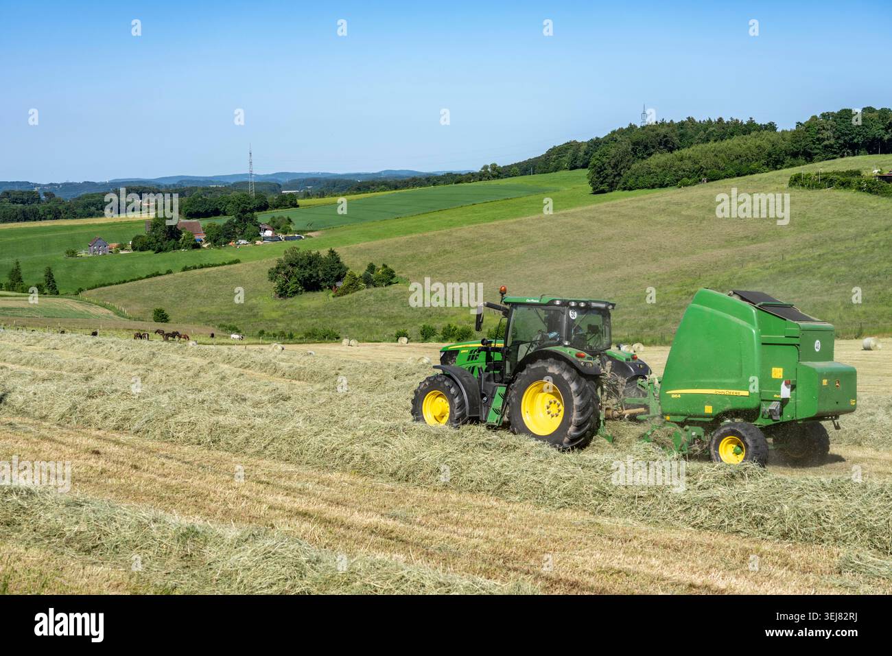Heuerzeugung im Wodan Valley zieht Ein John Deere-Traktor eine John Deere-Rundballenpresse und sammelt das Erntegut – das zuvor gemähte, getrocknete A-Stroh Stockfoto