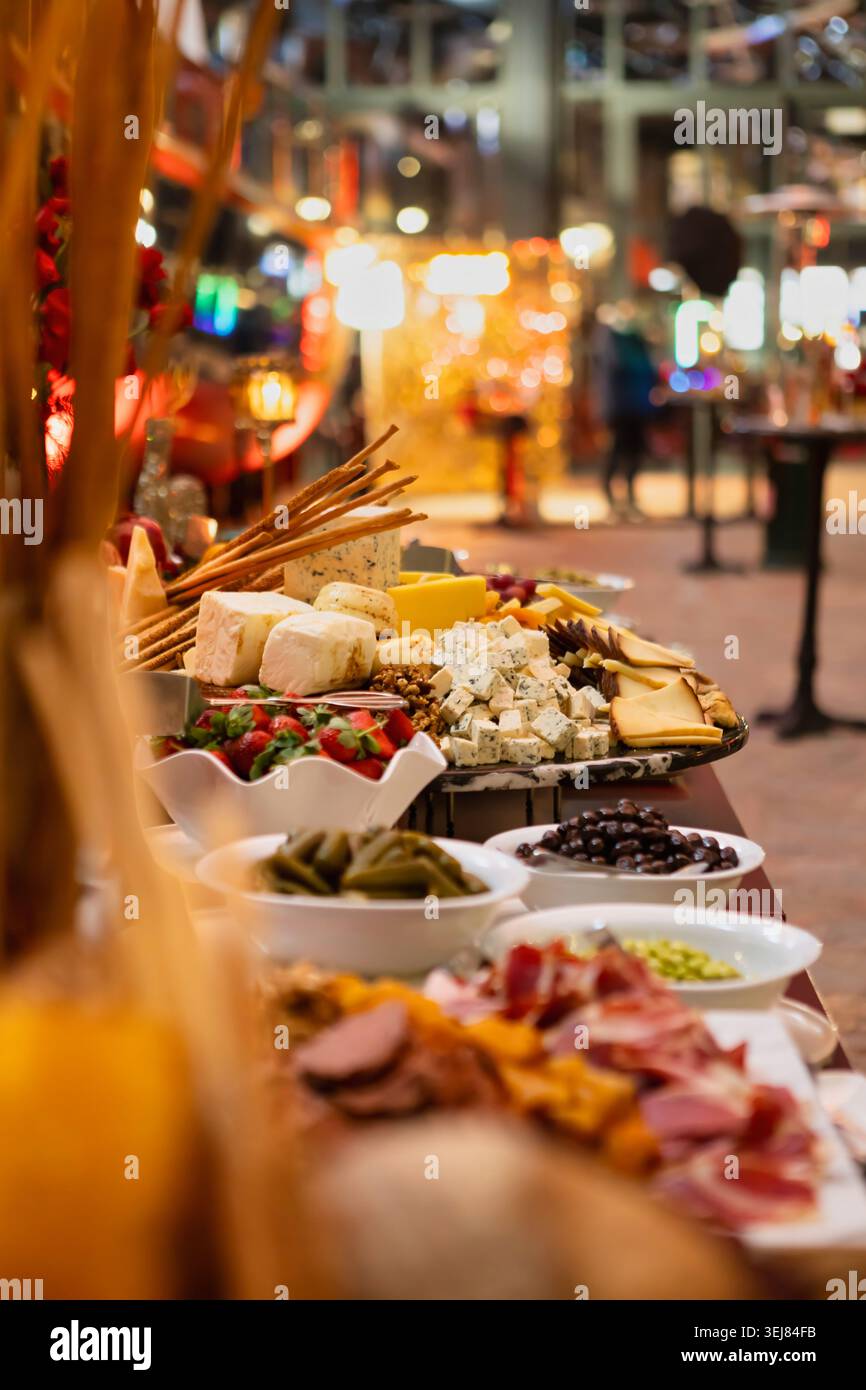 Ein langer Buffettisch gesäumt mit Käseplatten, Wurstwaren, Oliven, Dolma, Erdbeeren, und Brotstangen bei einer eleganten Indoor-Abendveranstaltung. Stockfoto