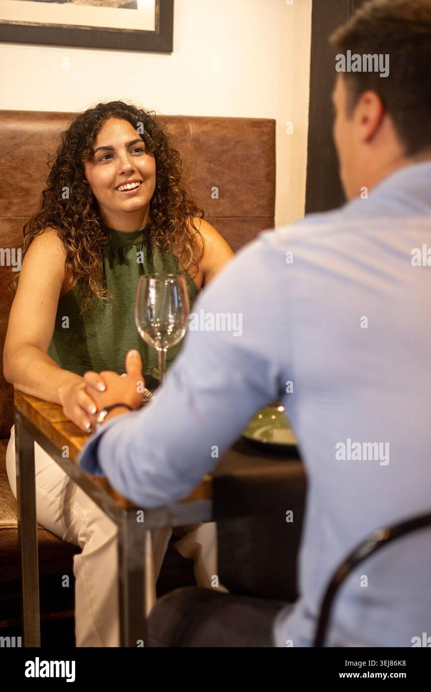Eine junge Frau, die ein angenehmes Gespräch während eines Dinner-Dates in einem gemütlichen Restaurant genießt. Warmes Ambiente, entspannte Atmosphäre und authentisches intera Stockfoto